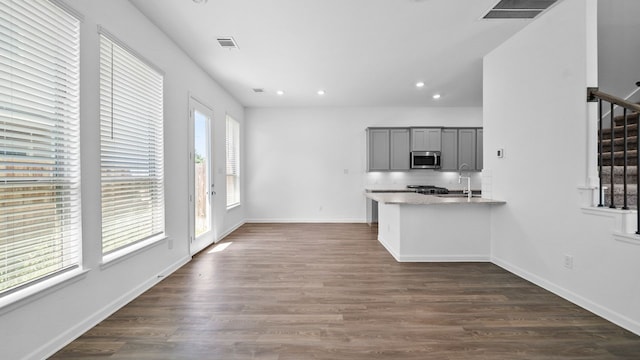 kitchen featuring gray cabinetry, light stone counters, dark hardwood / wood-style floors, backsplash, and kitchen peninsula