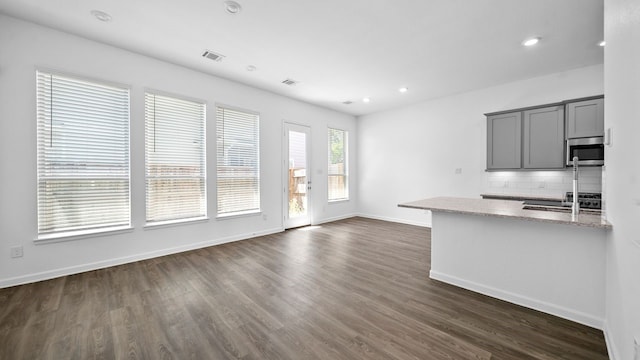 kitchen with light stone countertops, tasteful backsplash, gray cabinetry, dark wood-type flooring, and sink