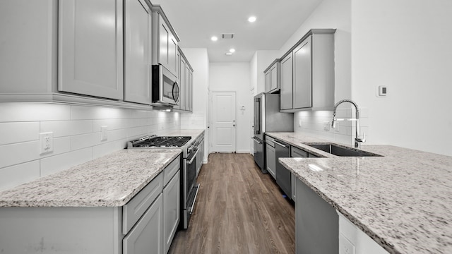 kitchen featuring light stone countertops, appliances with stainless steel finishes, sink, gray cabinets, and dark hardwood / wood-style floors