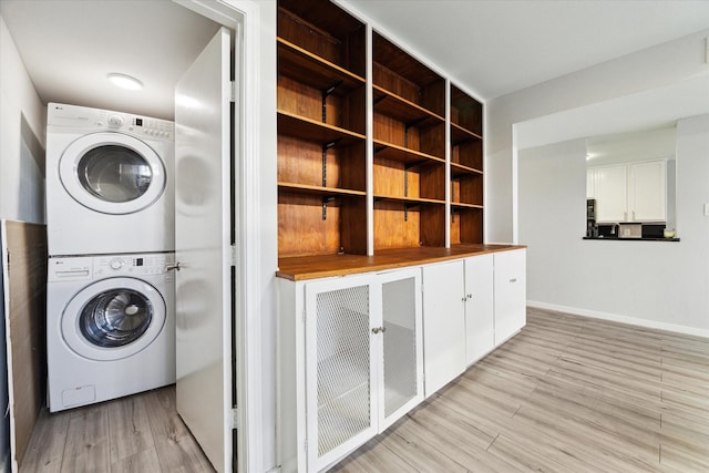 laundry area with light hardwood / wood-style floors and stacked washing maching and dryer