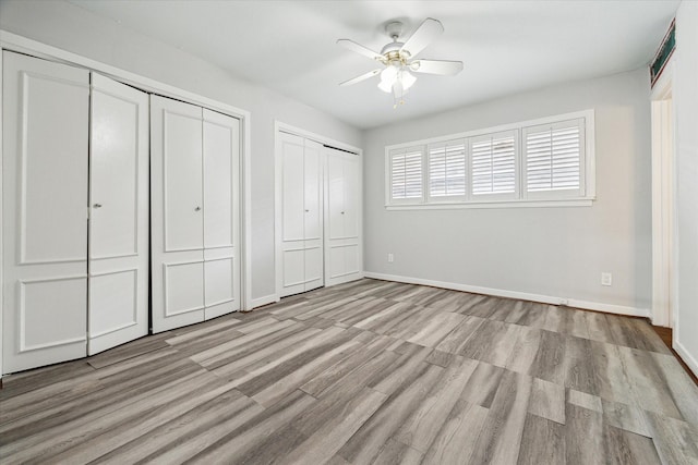 unfurnished bedroom with ceiling fan, two closets, and light wood-type flooring