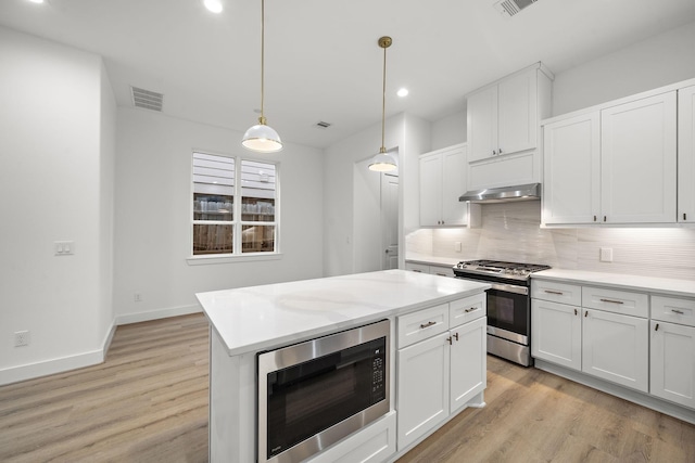 kitchen featuring white cabinets, decorative light fixtures, built in microwave, and stainless steel gas range