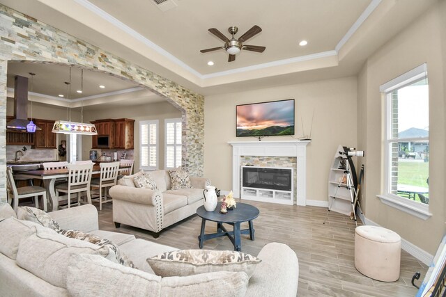 living room with a tray ceiling, plenty of natural light, crown molding, and ceiling fan