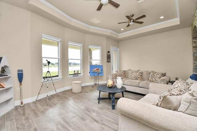 living room with ceiling fan, a raised ceiling, ornamental molding, and light hardwood / wood-style flooring