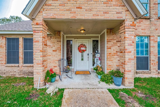 entrance to property featuring brick siding and a shingled roof