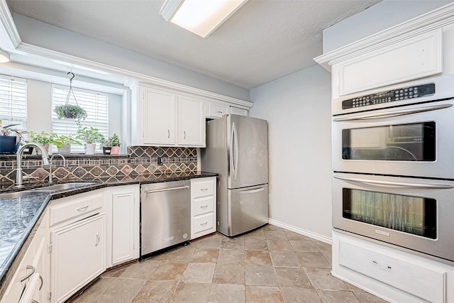 kitchen featuring decorative backsplash, appliances with stainless steel finishes, white cabinets, a sink, and dark stone counters