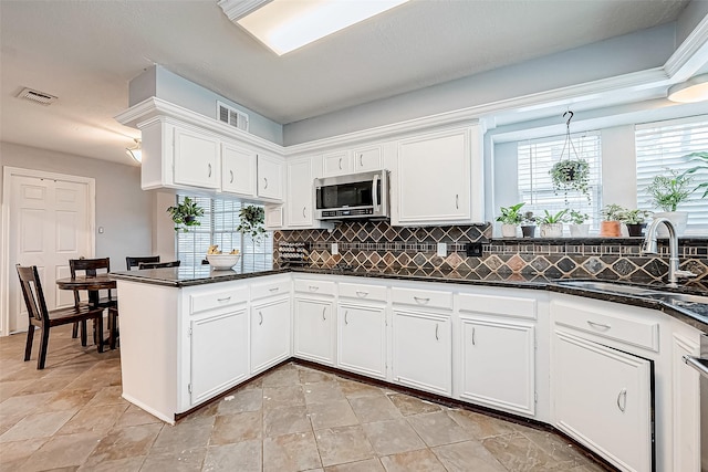 kitchen with backsplash, dark stone counters, white cabinets, sink, and kitchen peninsula