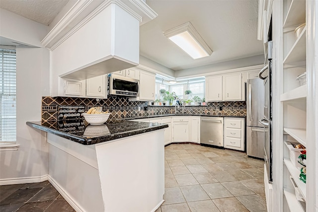 kitchen featuring stainless steel appliances, tasteful backsplash, white cabinetry, a sink, and a peninsula