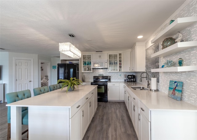 kitchen with a kitchen bar, sink, white cabinetry, decorative light fixtures, and black appliances