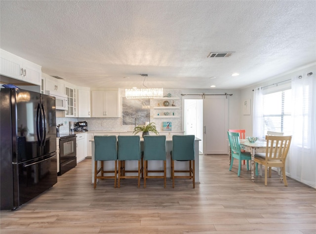 kitchen with a center island, hanging light fixtures, a barn door, black appliances, and white cabinets