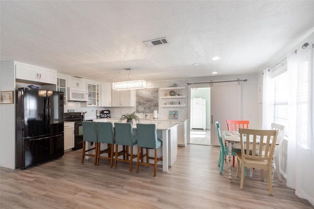 kitchen with white cabinetry, pendant lighting, a kitchen island, black appliances, and a barn door