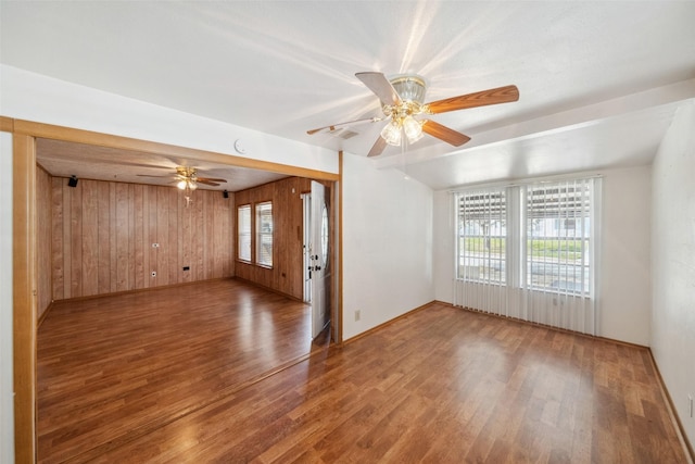 unfurnished living room with ceiling fan, wood walls, and wood-type flooring