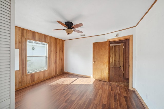 spare room featuring ceiling fan, dark hardwood / wood-style flooring, crown molding, and wood walls