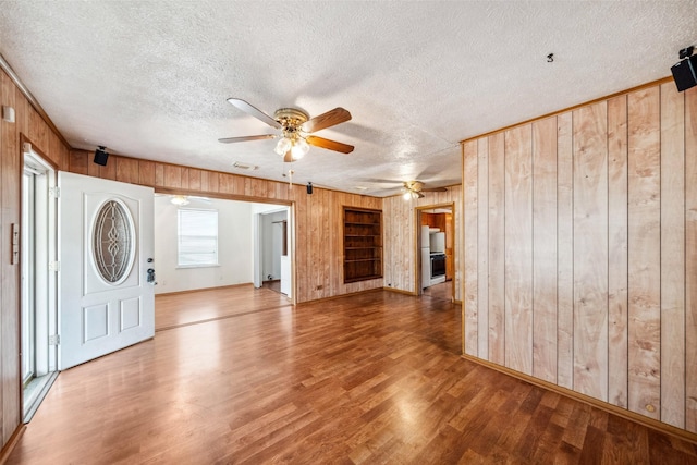 foyer entrance featuring a textured ceiling, hardwood / wood-style flooring, ceiling fan, and wooden walls