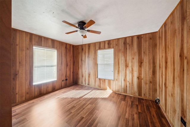 empty room with ceiling fan, dark wood-type flooring, and wood walls