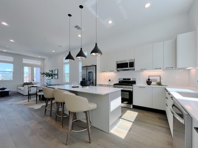 kitchen with french doors, stainless steel appliances, pendant lighting, white cabinets, and light wood-type flooring