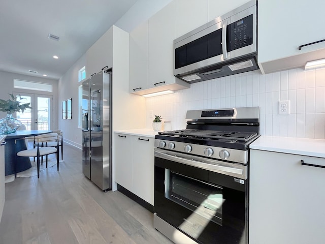 kitchen with backsplash, french doors, light wood-type flooring, white cabinetry, and stainless steel appliances