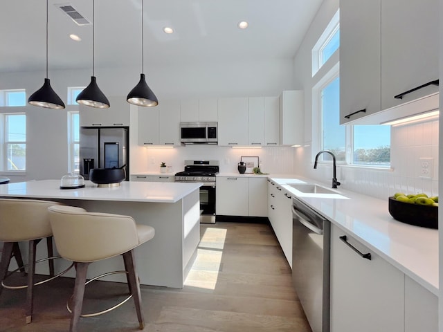 kitchen with sink, white cabinets, stainless steel appliances, and decorative light fixtures