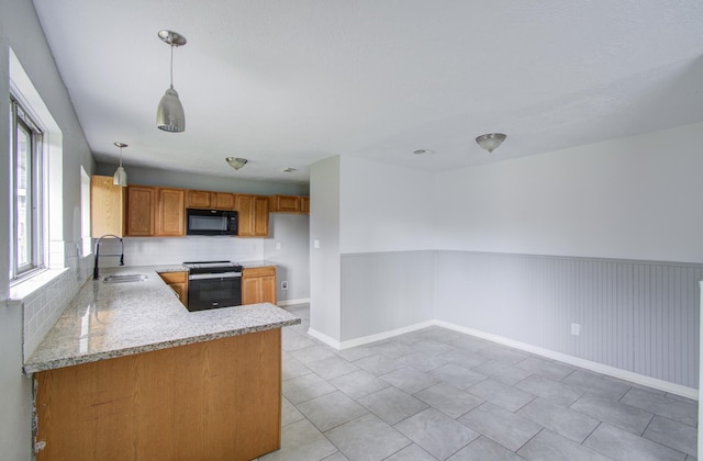 kitchen featuring kitchen peninsula, light stone counters, sink, black appliances, and decorative light fixtures