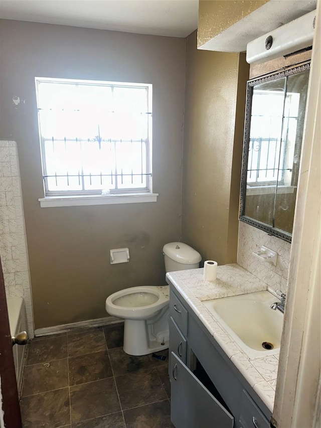 bathroom with a tub to relax in, vanity, a healthy amount of sunlight, and toilet