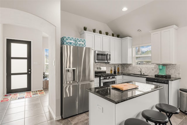 kitchen with appliances with stainless steel finishes, dark stone countertops, white cabinets, a kitchen island, and lofted ceiling