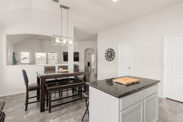 kitchen featuring a center island, dark stone counters, lofted ceiling, decorative light fixtures, and white cabinets