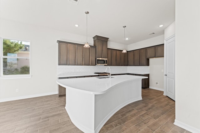 kitchen featuring pendant lighting, backsplash, dark brown cabinets, and an island with sink