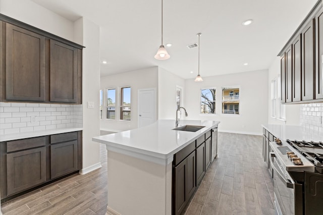 kitchen featuring stainless steel range oven, sink, hanging light fixtures, an island with sink, and decorative backsplash