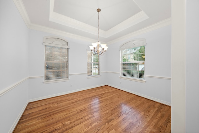 empty room with hardwood / wood-style flooring, ornamental molding, an inviting chandelier, and a tray ceiling