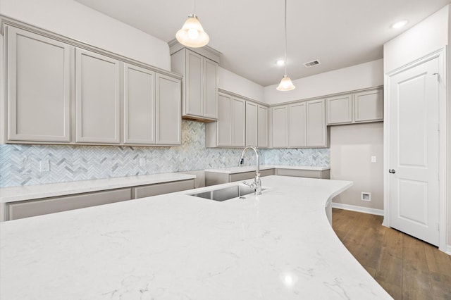 kitchen featuring pendant lighting, gray cabinetry, sink, dark hardwood / wood-style floors, and light stone countertops