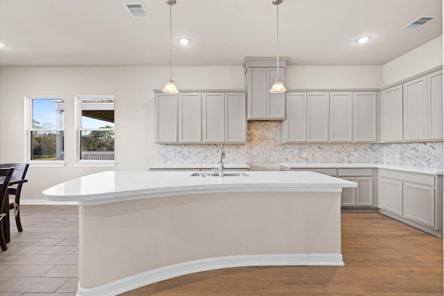 kitchen featuring gray cabinetry, sink, and an island with sink