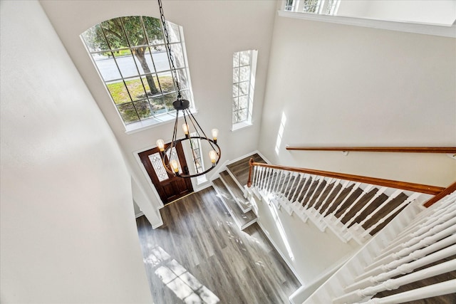 stairway featuring a wealth of natural light, a towering ceiling, hardwood / wood-style flooring, and an inviting chandelier