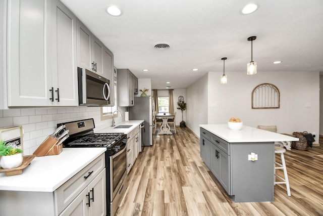 kitchen featuring a kitchen bar, appliances with stainless steel finishes, light wood-type flooring, gray cabinetry, and pendant lighting