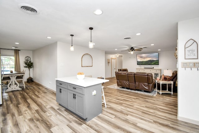 kitchen featuring a kitchen breakfast bar, light hardwood / wood-style flooring, pendant lighting, gray cabinets, and a kitchen island