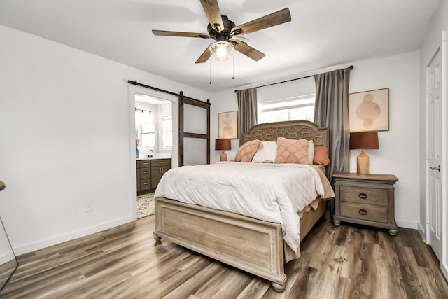 bedroom featuring ceiling fan, a barn door, dark wood-type flooring, and ensuite bath