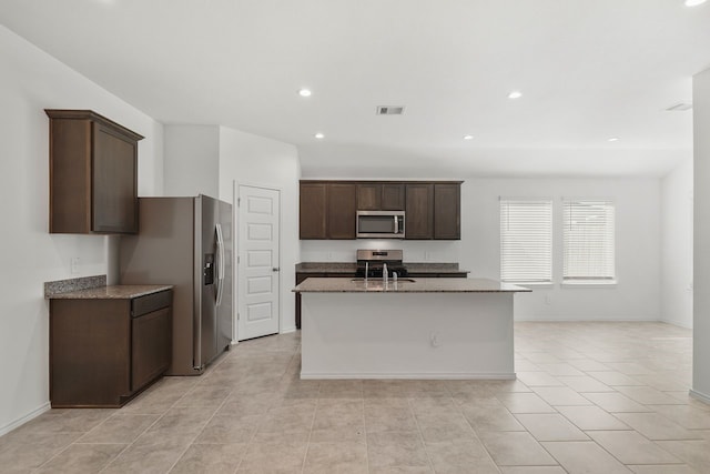 kitchen featuring dark brown cabinetry, stone countertops, a kitchen island with sink, light tile patterned flooring, and appliances with stainless steel finishes