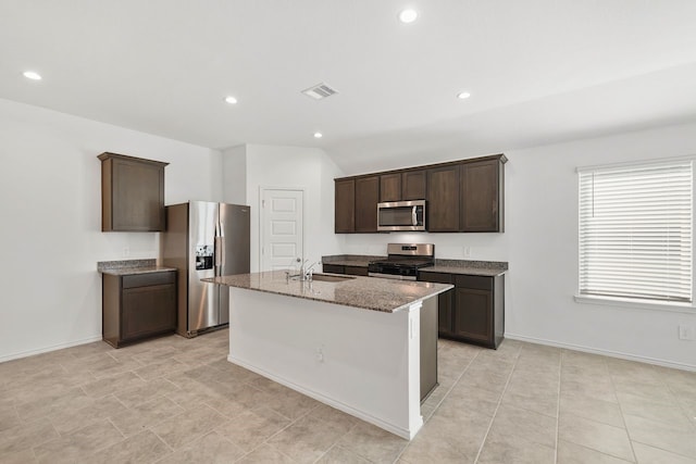 kitchen with light stone countertops, sink, a center island with sink, dark brown cabinets, and appliances with stainless steel finishes