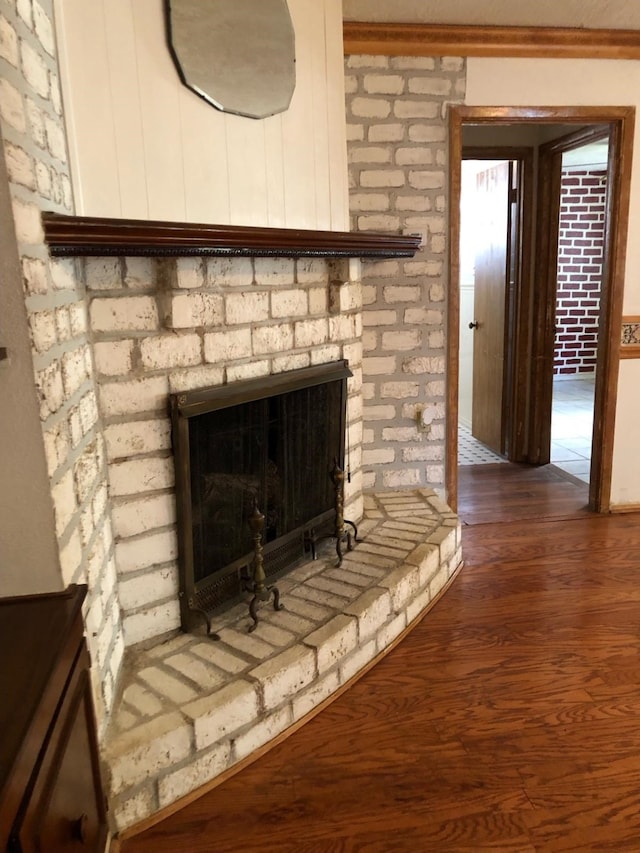 room details featuring wood-type flooring, a brick fireplace, and crown molding