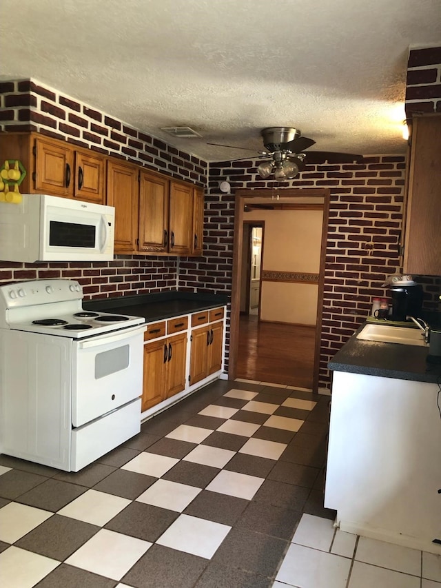 kitchen with a textured ceiling, sink, brick wall, and white appliances