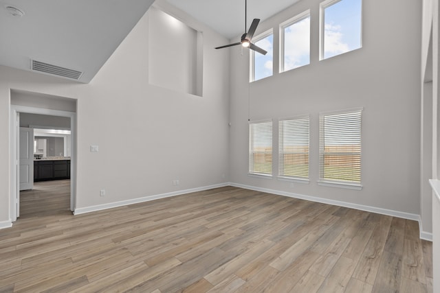 unfurnished living room with a healthy amount of sunlight, a high ceiling, and light hardwood / wood-style flooring