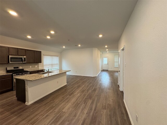 kitchen with a kitchen island with sink, sink, light stone countertops, dark brown cabinetry, and stainless steel appliances