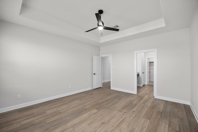 unfurnished bedroom with a tray ceiling, a walk in closet, ceiling fan, and light wood-type flooring