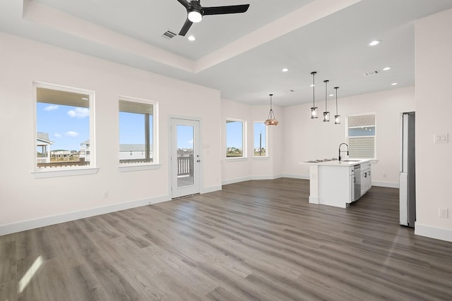 unfurnished living room with a raised ceiling, a wealth of natural light, ceiling fan, and dark hardwood / wood-style floors