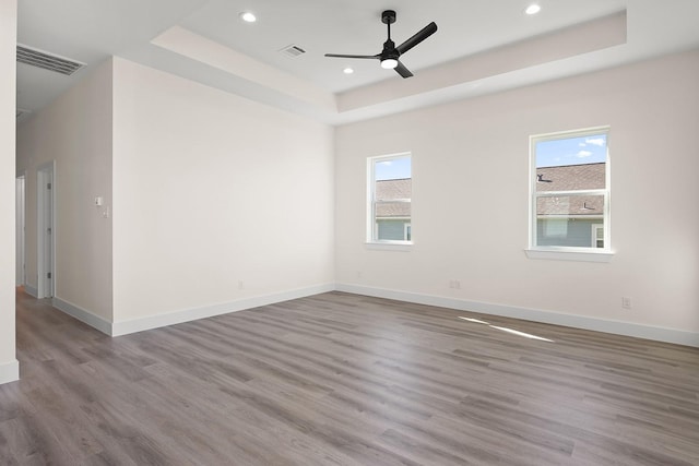 unfurnished room with ceiling fan, light hardwood / wood-style floors, and a tray ceiling