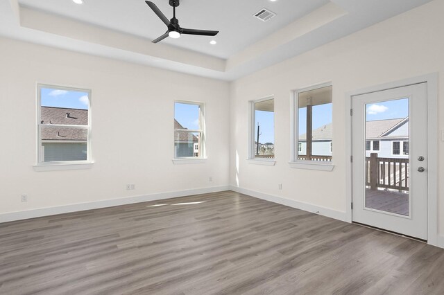 empty room with hardwood / wood-style flooring, plenty of natural light, ceiling fan, and a raised ceiling