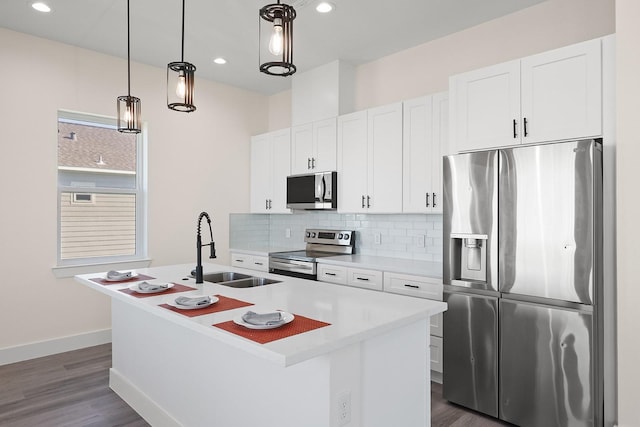 kitchen with stainless steel appliances, sink, white cabinetry, hanging light fixtures, and an island with sink