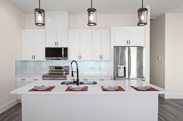 kitchen with a center island with sink, sink, appliances with stainless steel finishes, decorative light fixtures, and white cabinetry