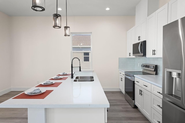 kitchen featuring stainless steel appliances, sink, decorative light fixtures, white cabinetry, and an island with sink