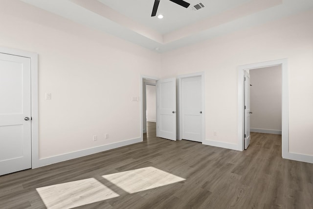 unfurnished bedroom featuring a tray ceiling, ceiling fan, and dark wood-type flooring