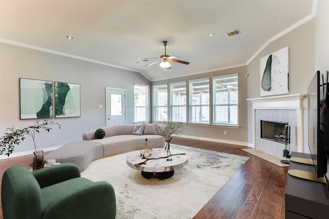 living room with lofted ceiling, ceiling fan, dark hardwood / wood-style floors, a tiled fireplace, and ornamental molding